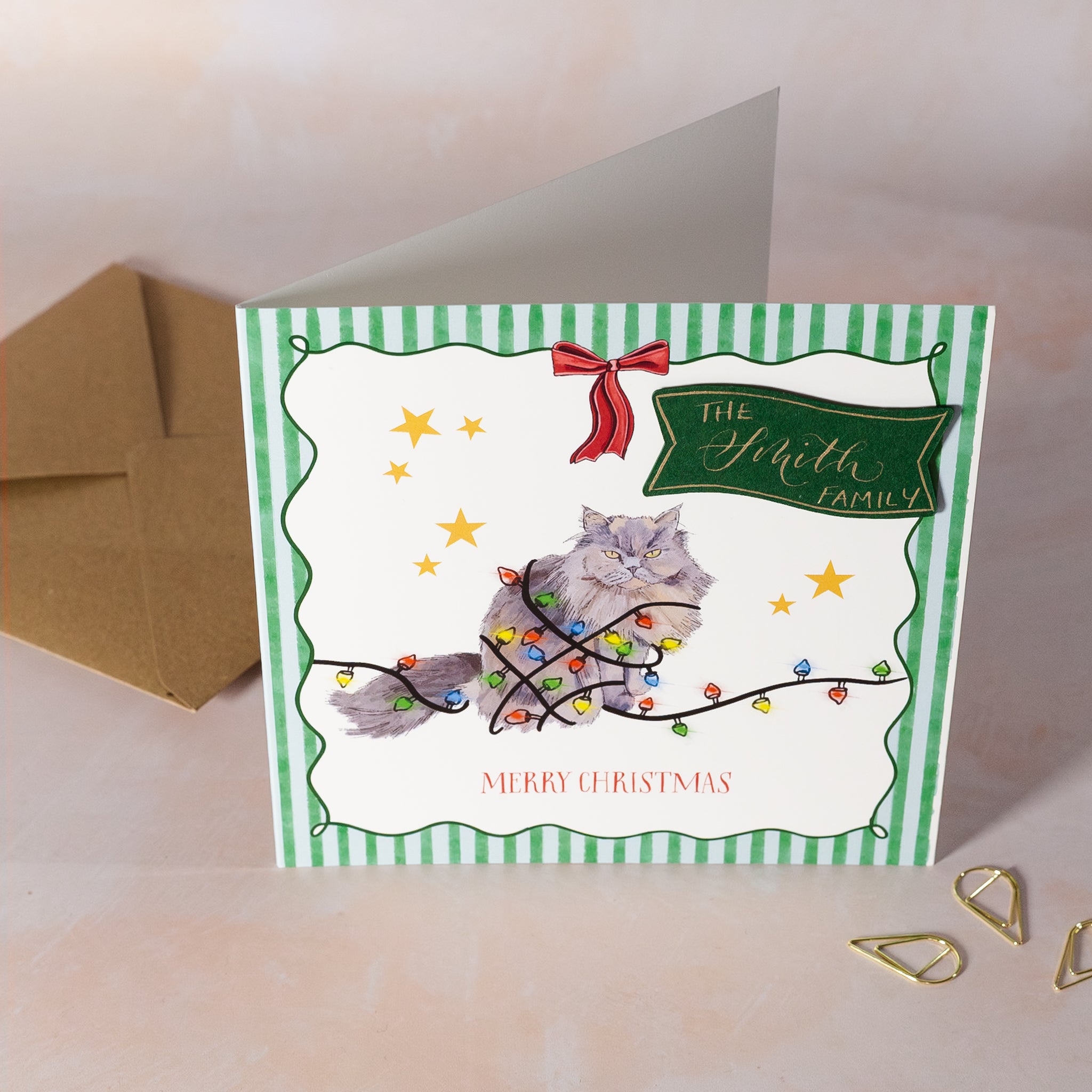 Christmas card with a cat tangled in lights, personalised name on green card with gold calligraphy