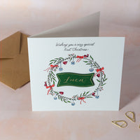 Personalised wreath Christmas card on blue background for boy's first Christmas.