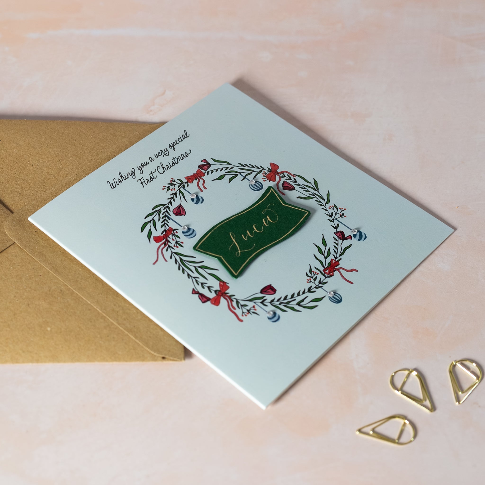 Christmas card with wreath design and calligraphy name in middle on green card with gold ink.