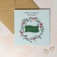 Personalised greeting card with festive wreath design for baby boy's first Christmas.