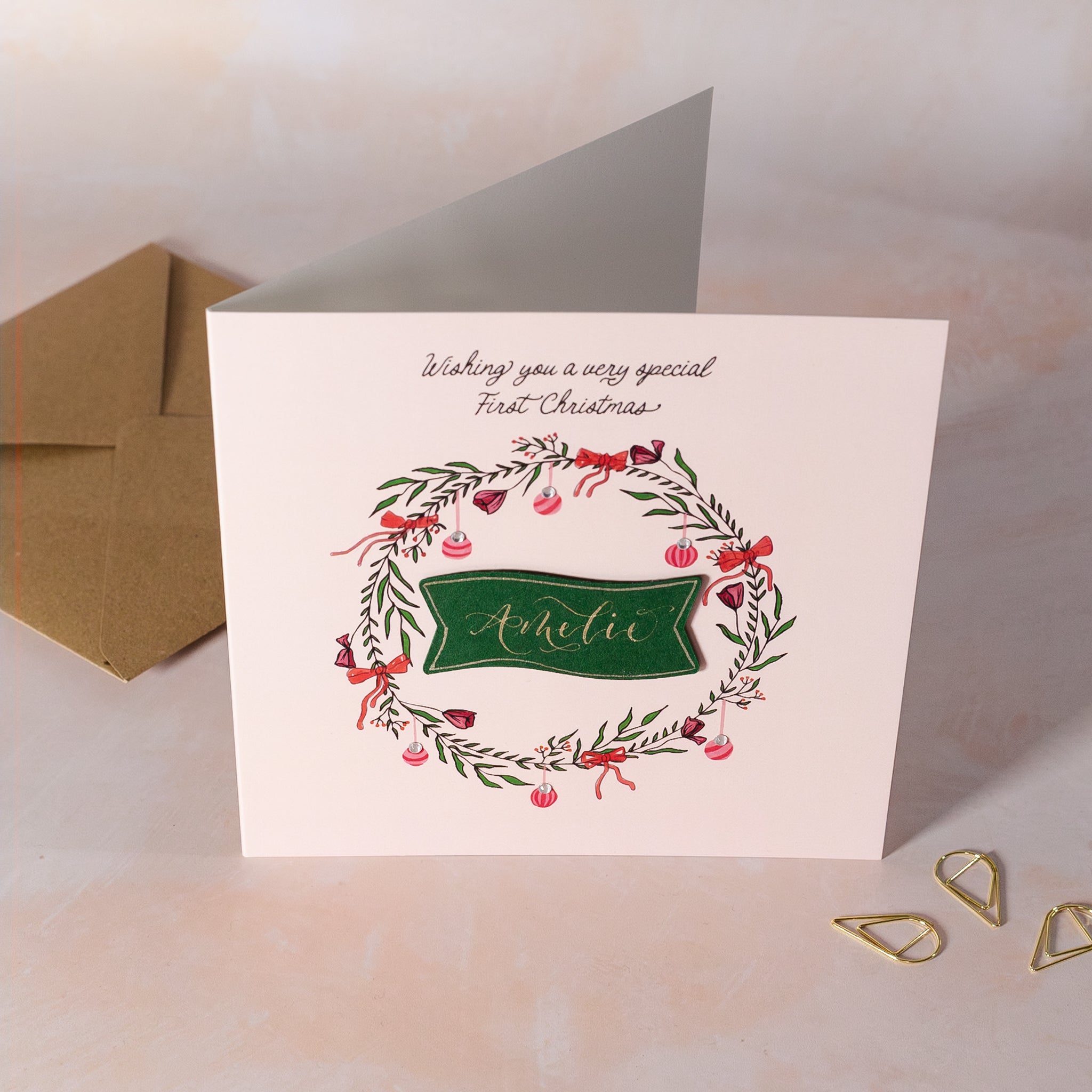 Christmas card with floral wreath and personalised name on a pink background