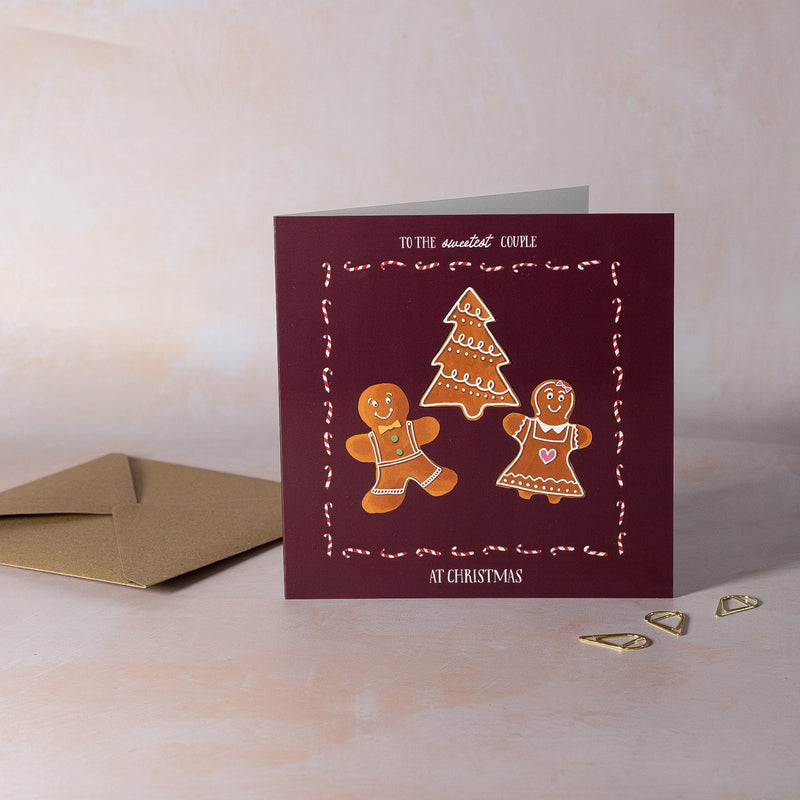 Greeting card with gingerbread men and Christmas tree design burgundy background with candy cane border
