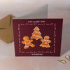 Christmas card with gingerbread men and a tree on a maroon background, with a brown envelope.