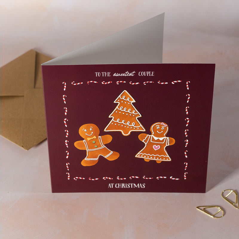 Christmas card with gingerbread men and a tree on a maroon background, with a brown envelope.