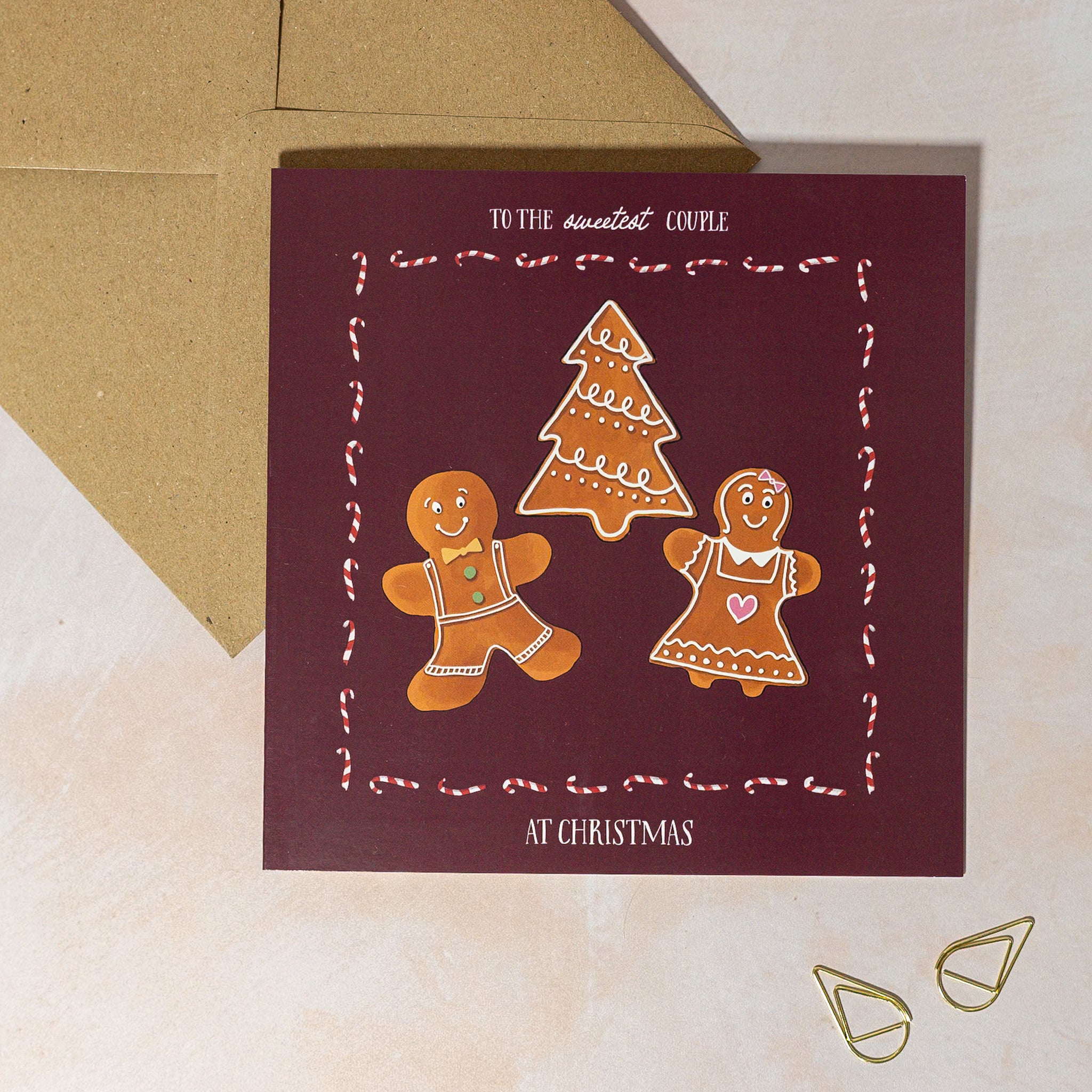 Christmas card with gingerbread men and a festive tree on a maroon background, with candy cane border.