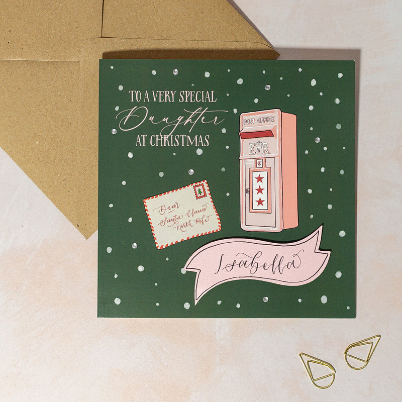 Personalised Christmas card with a pink mailbox illustration on a green background with snow in background and handwritten calligraphy name
