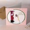 Christmas card with a red postbox and robin design on a pink striped background
