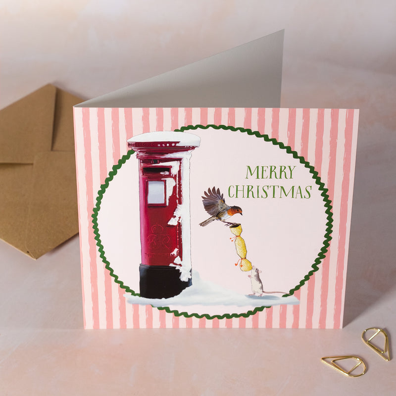 Christmas card with a red postbox and robin design on a pink striped background